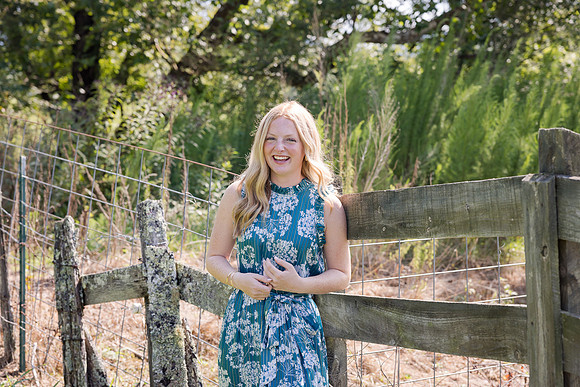 Beautiful senior in Hiawassee GA in front of an old wooden fence in a beautiful dress smiling for her senior portraits